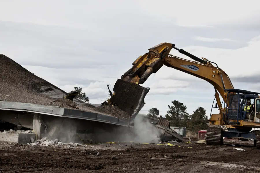 Excavator pulling down the roof of a building, dust rising