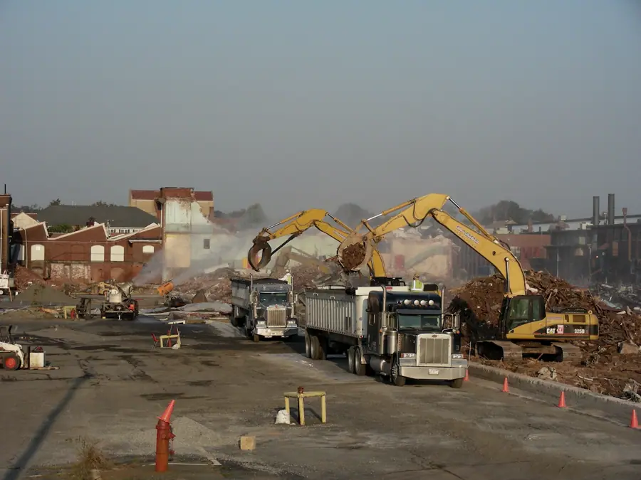 Excavators loading demolition debris into trucks on a cleared industrial site